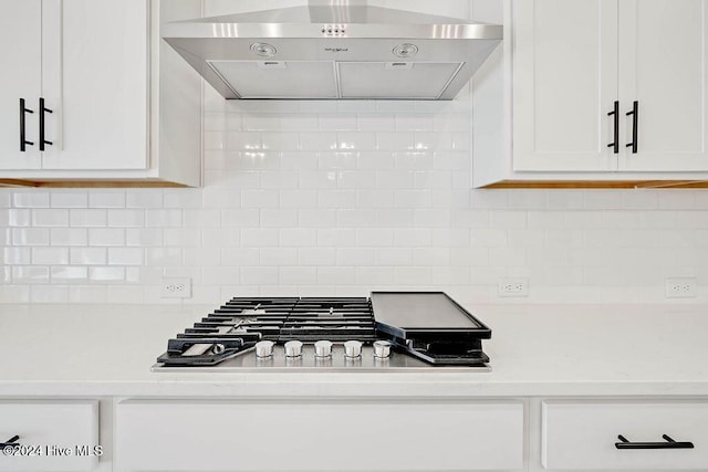 kitchen with white cabinetry, under cabinet range hood, light stone counters, backsplash, and stainless steel gas stovetop