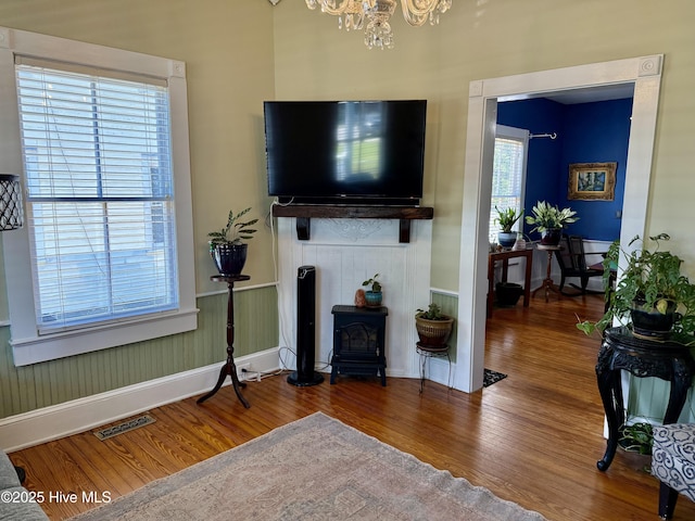 living area featuring visible vents, a wood stove, wood finished floors, baseboards, and a chandelier