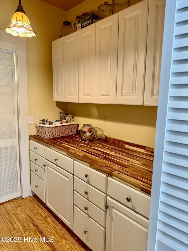 kitchen with white cabinets, decorative light fixtures, butcher block countertops, and light wood finished floors