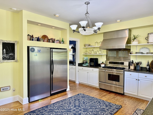 kitchen with open shelves, light wood finished floors, an inviting chandelier, stainless steel appliances, and wall chimney exhaust hood