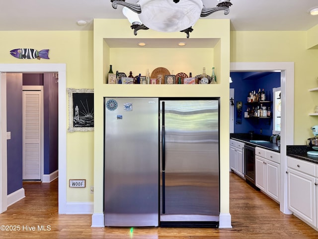 kitchen featuring white cabinets, dark countertops, stainless steel refrigerator, beverage cooler, and wood finished floors