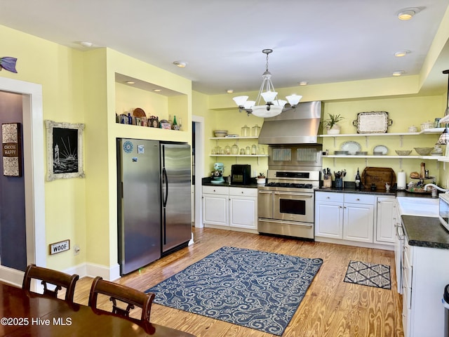 kitchen with wall chimney range hood, white cabinets, open shelves, dark countertops, and stainless steel appliances