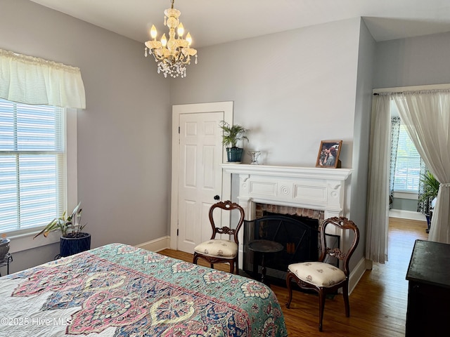 bedroom with baseboards, a chandelier, wood finished floors, and a fireplace