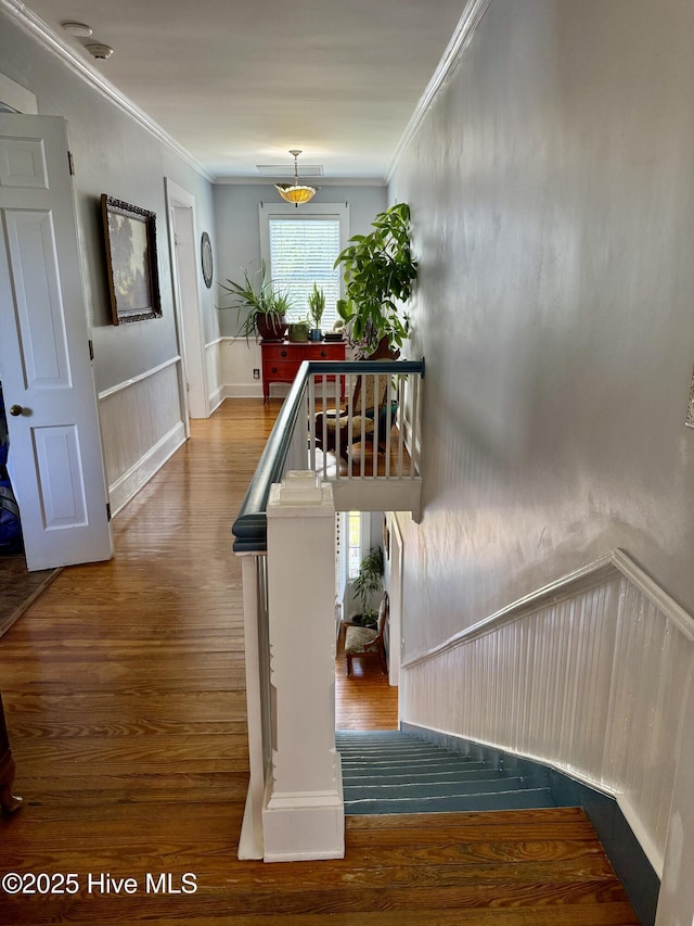 stairs featuring crown molding, wainscoting, and wood finished floors