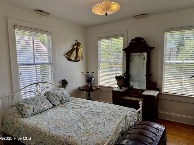 bedroom featuring baseboards, visible vents, multiple windows, and wood finished floors