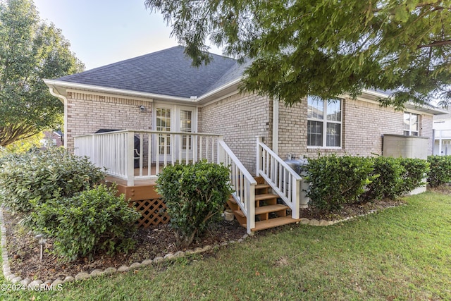 rear view of property featuring roof with shingles, a yard, a deck, and brick siding