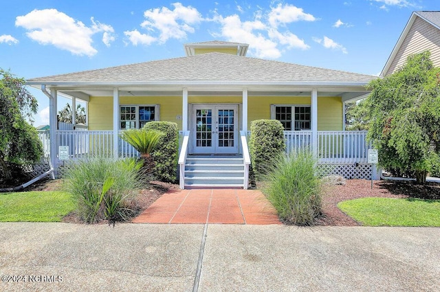 view of exterior entry with a shingled roof, french doors, and covered porch