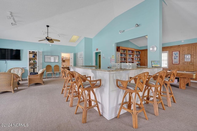 kitchen with ceiling fan, wooden walls, light carpet, and a breakfast bar