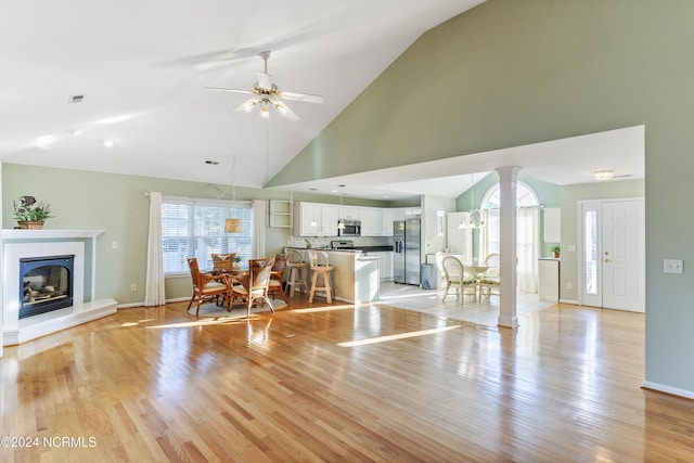 living room featuring ceiling fan, a glass covered fireplace, baseboards, light wood-type flooring, and ornate columns