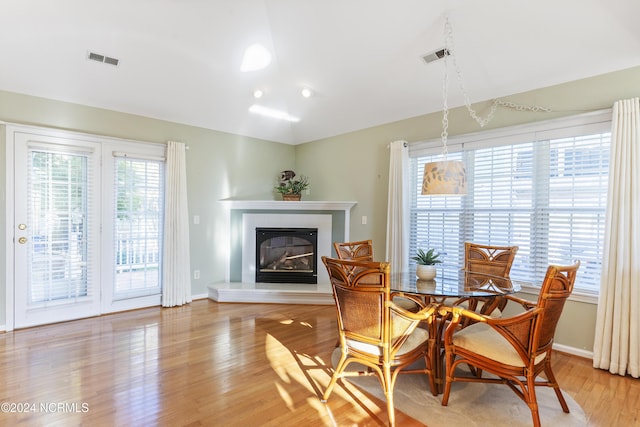 dining room with visible vents, a glass covered fireplace, lofted ceiling, baseboards, and light wood-type flooring