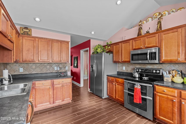 kitchen featuring lofted ceiling, dark countertops, baseboards, a sink, and appliances with stainless steel finishes
