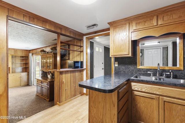 kitchen with black microwave, dark countertops, a sink, light wood finished floors, and wooden walls