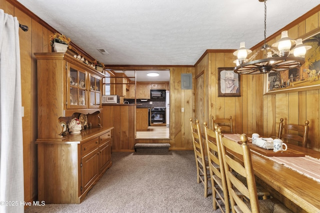 carpeted dining room with wooden walls, a textured ceiling, an inviting chandelier, and visible vents
