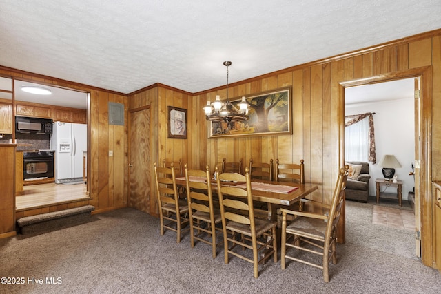 dining room with wooden walls, carpet flooring, a textured ceiling, and a chandelier