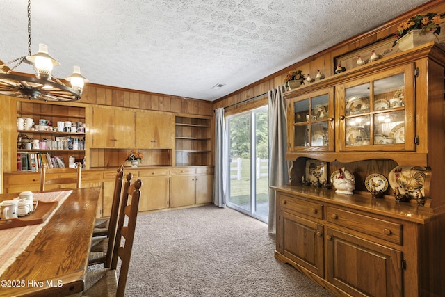 dining area featuring an inviting chandelier, a textured ceiling, crown molding, carpet floors, and wooden walls
