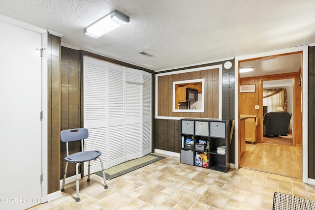 interior space with wooden walls, baseboards, a textured ceiling, and visible vents