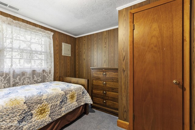 carpeted bedroom featuring a textured ceiling, visible vents, wood walls, and ornamental molding