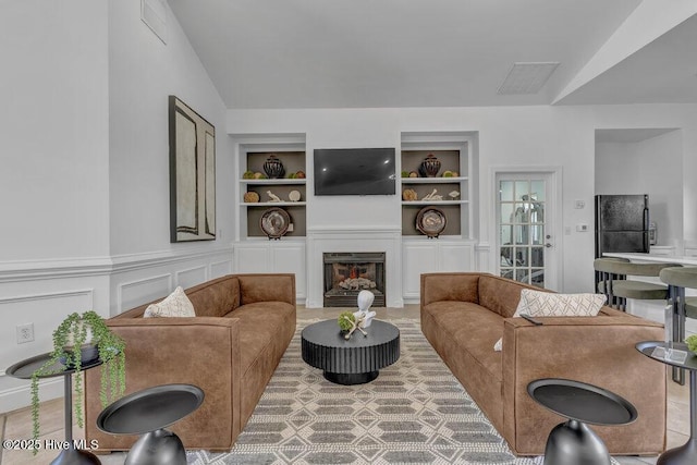 living room with vaulted ceiling, visible vents, a warm lit fireplace, and built in shelves