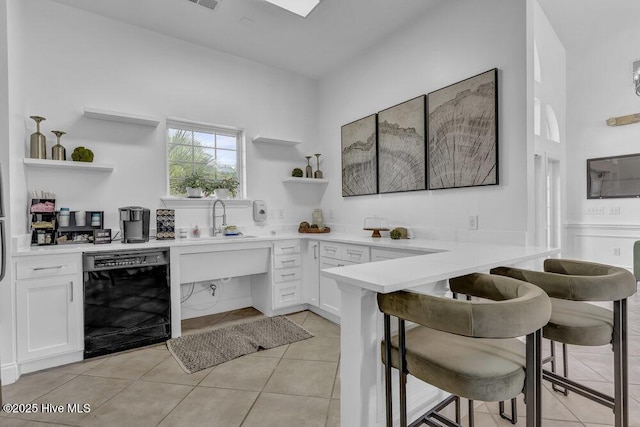 kitchen featuring a peninsula, a sink, open shelves, black dishwasher, and a kitchen breakfast bar