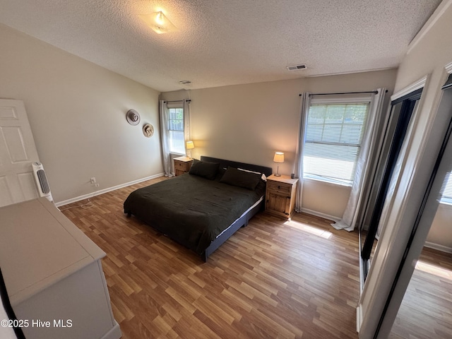 bedroom featuring baseboards, a textured ceiling, light wood finished floors, and visible vents