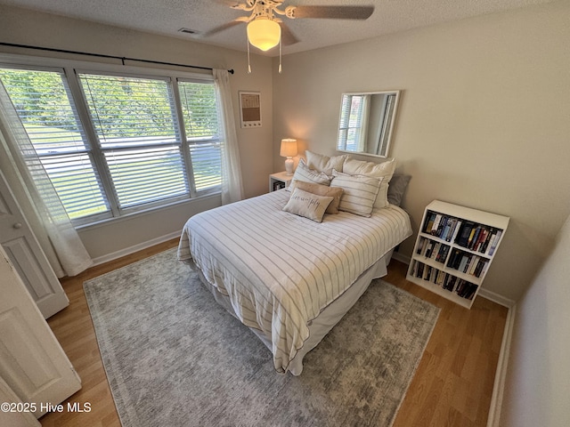 bedroom featuring visible vents, baseboards, ceiling fan, and wood finished floors