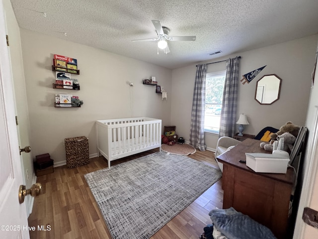 bedroom with visible vents, wood finished floors, baseboards, ceiling fan, and a textured ceiling