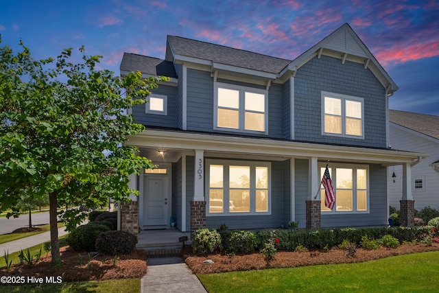 craftsman-style home featuring covered porch, a shingled roof, and a front lawn
