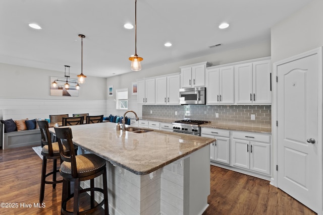 kitchen with stainless steel microwave, a sink, range, white cabinetry, and a wainscoted wall