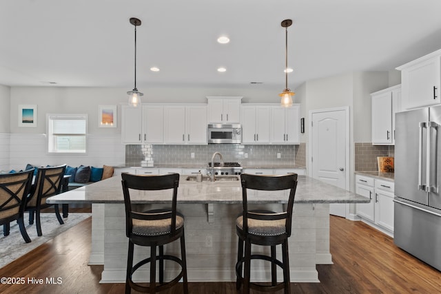 kitchen featuring appliances with stainless steel finishes, a center island with sink, a kitchen bar, light stone counters, and recessed lighting