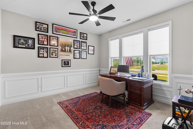 office space with light colored carpet, ceiling fan, wainscoting, and a decorative wall