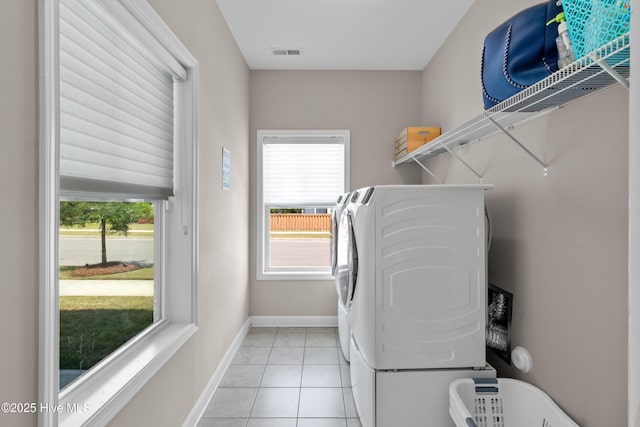 laundry area with washing machine and clothes dryer, plenty of natural light, light tile patterned flooring, and baseboards