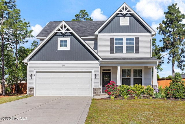 craftsman-style house featuring fence, stone siding, a front yard, covered porch, and driveway