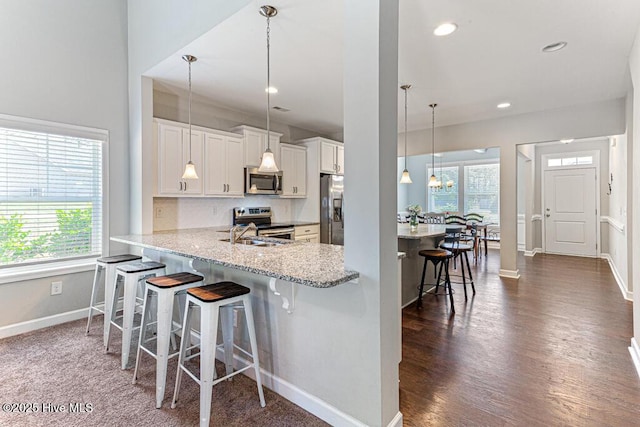 kitchen with pendant lighting, baseboards, a kitchen breakfast bar, white cabinets, and appliances with stainless steel finishes