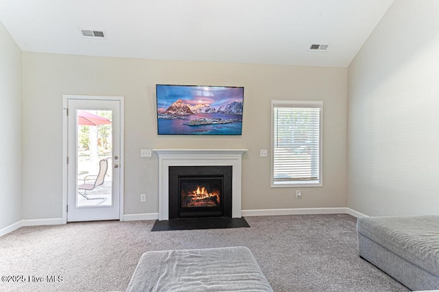 carpeted living area featuring baseboards, visible vents, and a fireplace with flush hearth