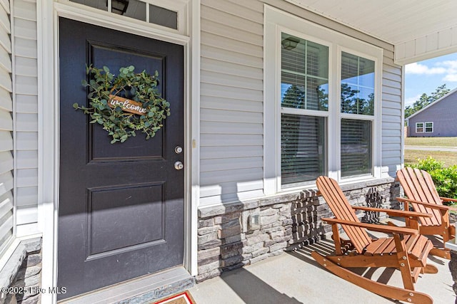 doorway to property featuring a porch and stone siding