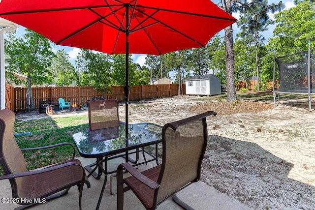 view of patio / terrace featuring a fenced backyard, outdoor dining area, a trampoline, and a storage unit