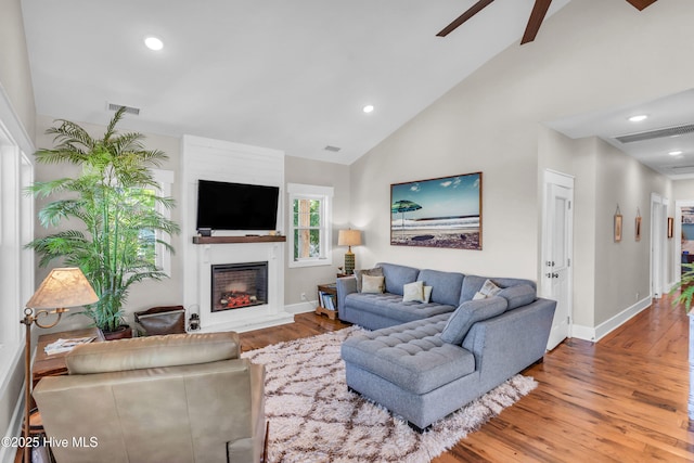 living room featuring visible vents, a glass covered fireplace, wood finished floors, baseboards, and a ceiling fan