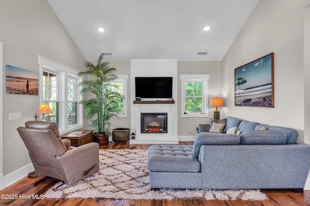 living room featuring visible vents, a glass covered fireplace, wood finished floors, baseboards, and high vaulted ceiling