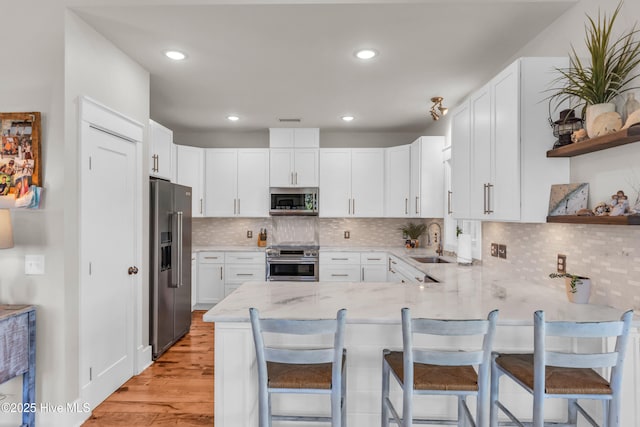 kitchen with light stone countertops, a sink, a peninsula, stainless steel appliances, and light wood-style flooring