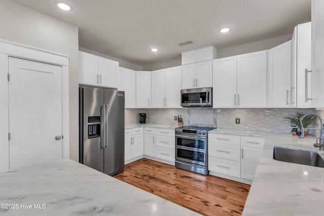 kitchen featuring visible vents, a sink, light stone counters, stainless steel appliances, and white cabinetry
