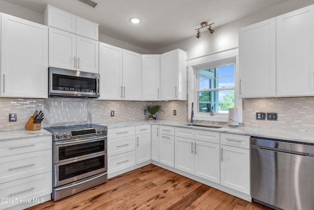 kitchen with light stone counters, a sink, white cabinetry, and stainless steel appliances