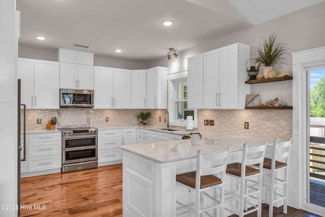 kitchen with a peninsula, light stone countertops, white cabinetry, a sink, and appliances with stainless steel finishes
