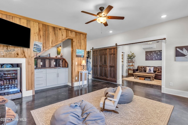living area featuring ceiling fan, a barn door, baseboards, an AC wall unit, and beverage cooler