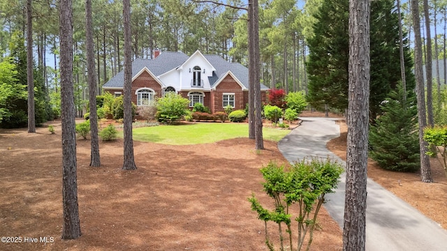 view of front of home with a front lawn, roof with shingles, driveway, and a chimney