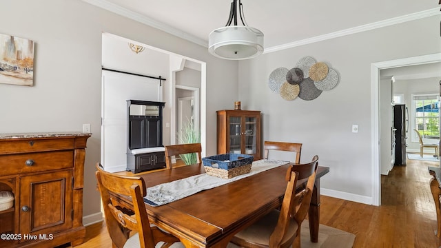 dining space featuring crown molding, baseboards, a barn door, and light wood finished floors