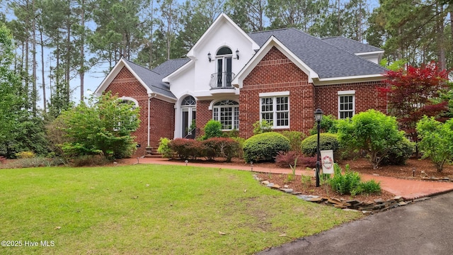 traditional home with stucco siding, brick siding, a front yard, and roof with shingles