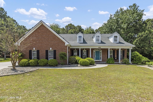 3733 Winstead Cir, Southport, NC 28461 - new england style home with covered porch, a shingled roof, a front yard, and brick siding