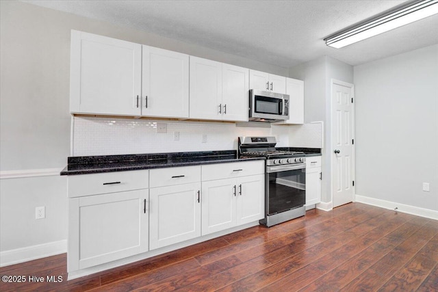 kitchen with white cabinetry, stainless steel appliances, baseboards, dark wood finished floors, and backsplash
