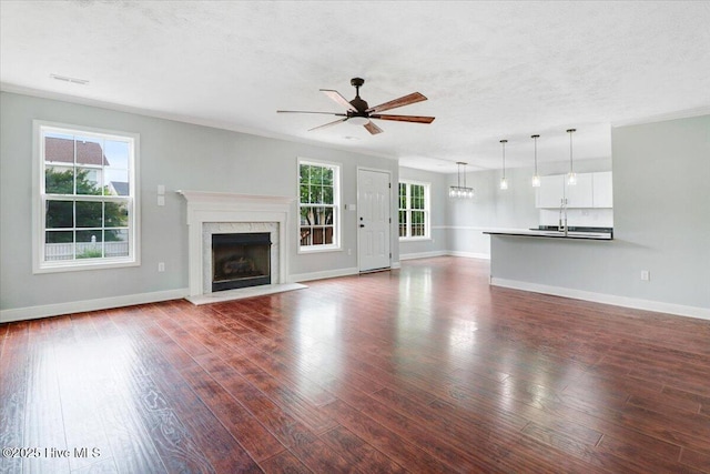 unfurnished living room with a premium fireplace, a ceiling fan, dark wood finished floors, and baseboards