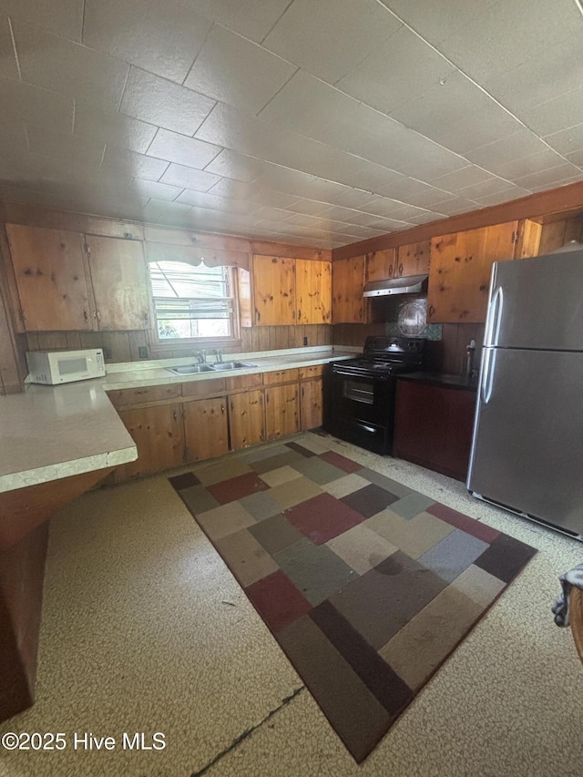 kitchen with brown cabinets, a sink, freestanding refrigerator, white microwave, and black range with electric stovetop